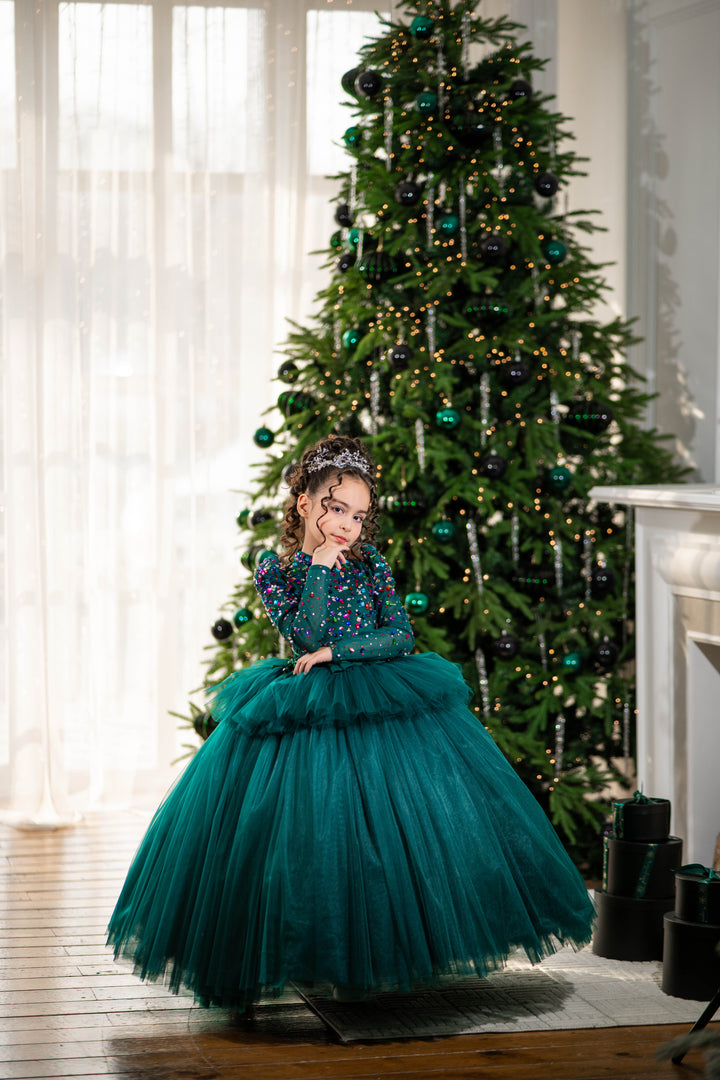 A child in a teal dress standing in front of a decorated Christmas tree.
