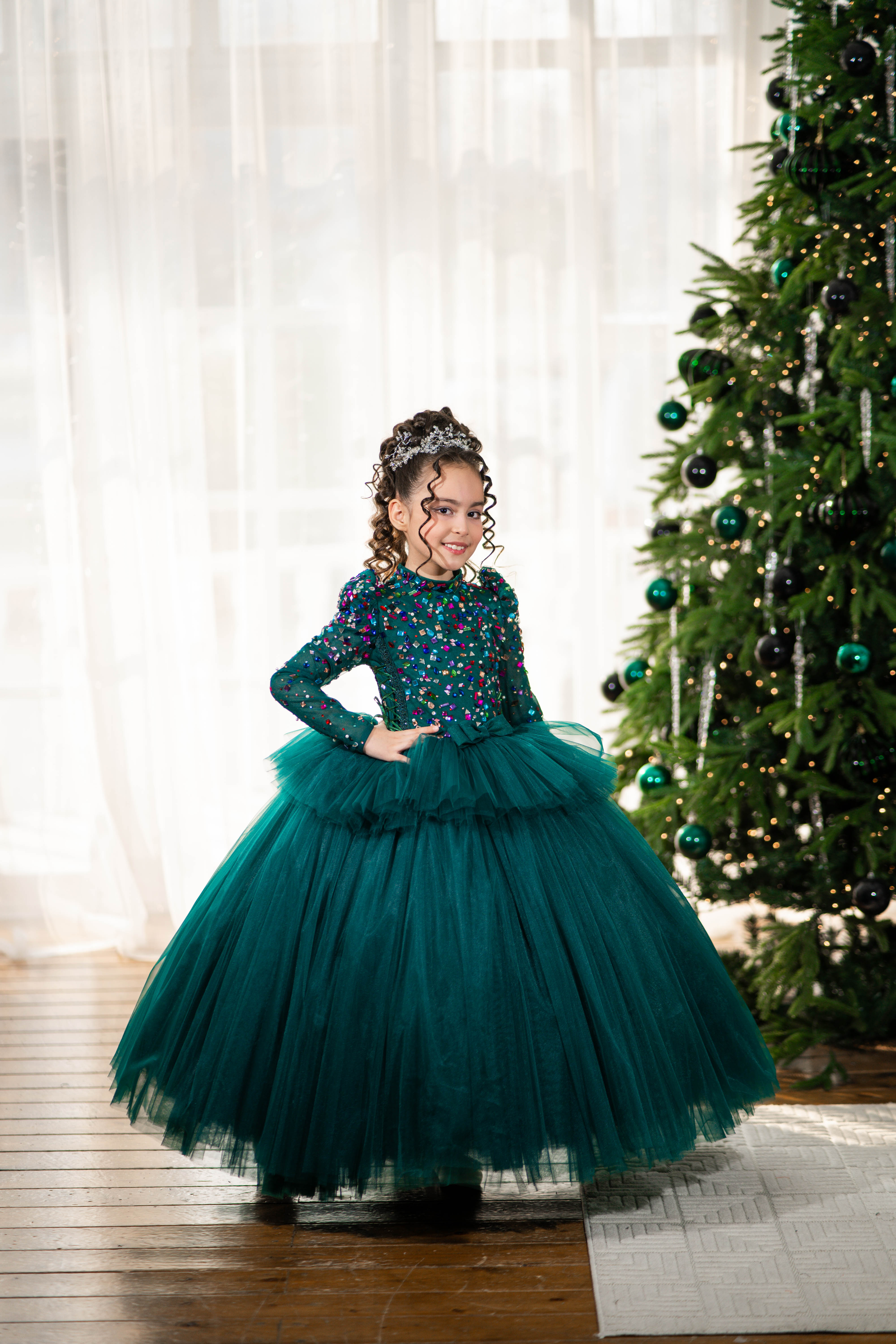 Young girl in a green dress standing in front of a decorated Christmas tree.