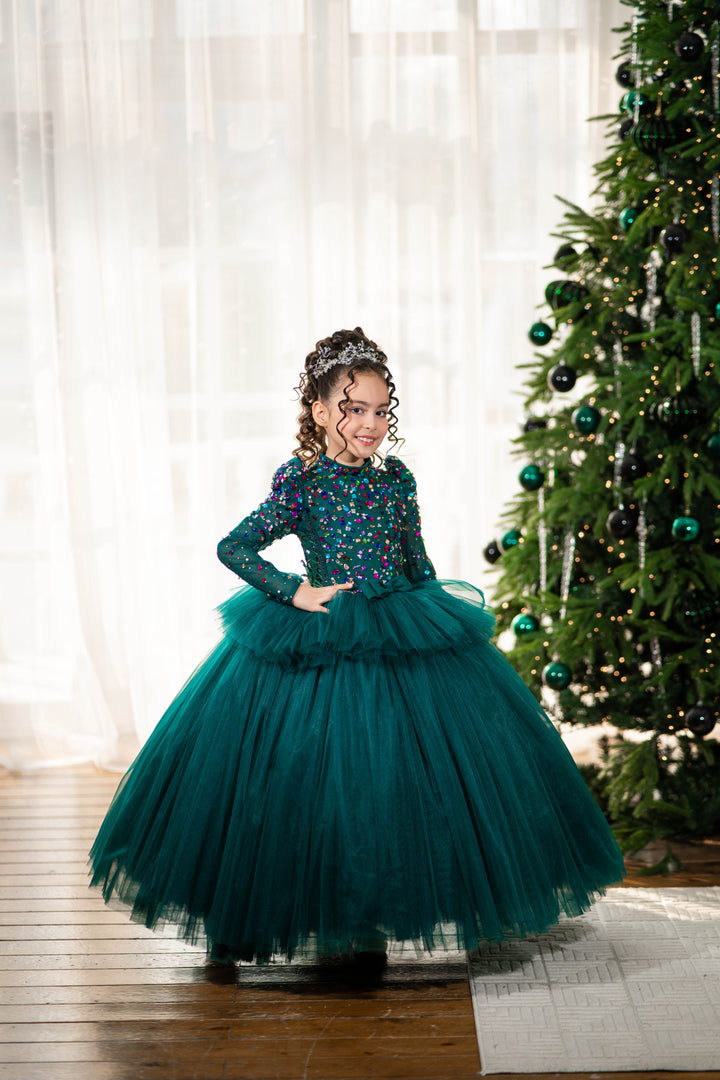 Young girl in a green dress standing in front of a decorated Christmas tree.