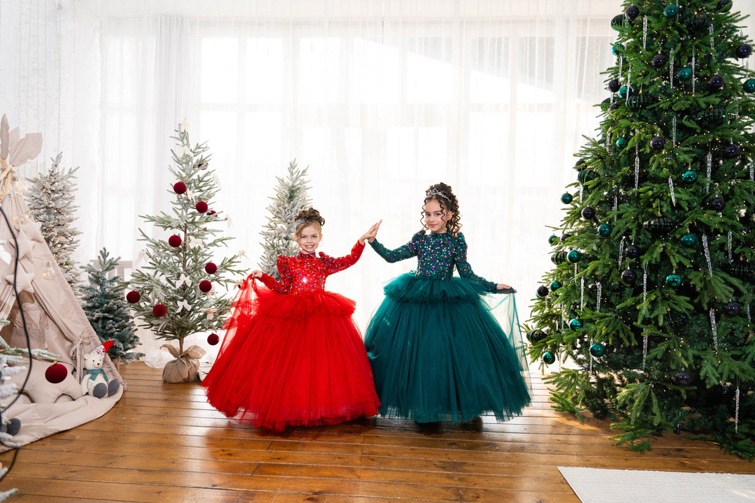 Two children in red and green dresses standing in a room with Christmas trees.