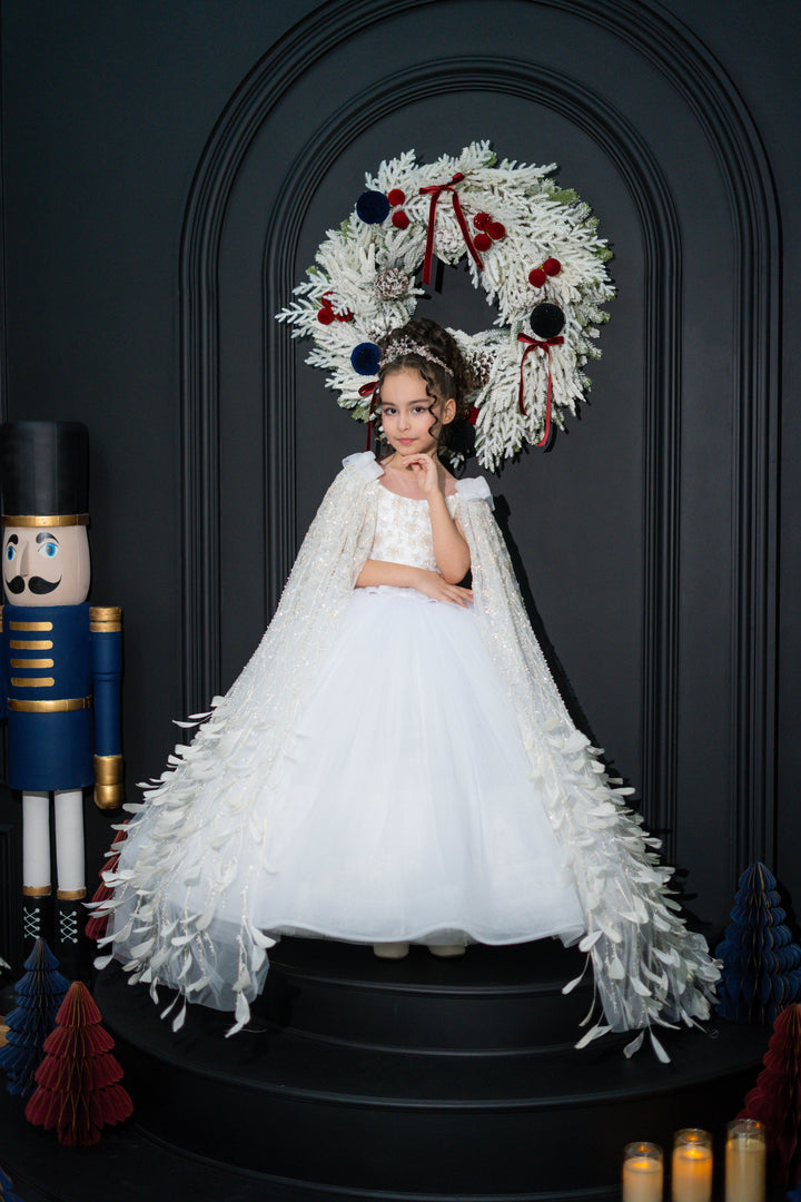 A child in a white dress standing in front of a decorative wreath on a dark background