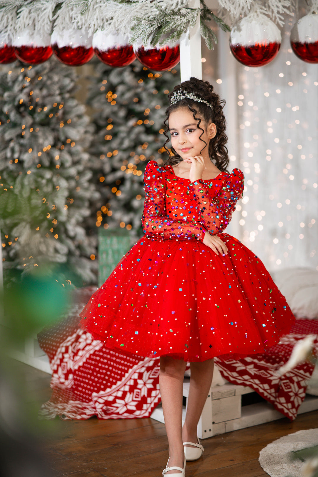 Young girl in a red dress with sequins standing in a festive setting with Christmas decorations.