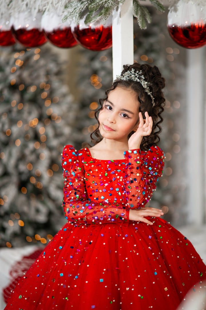 Young girl in a red dress with sequins standing in front of a decorated Christmas tree.