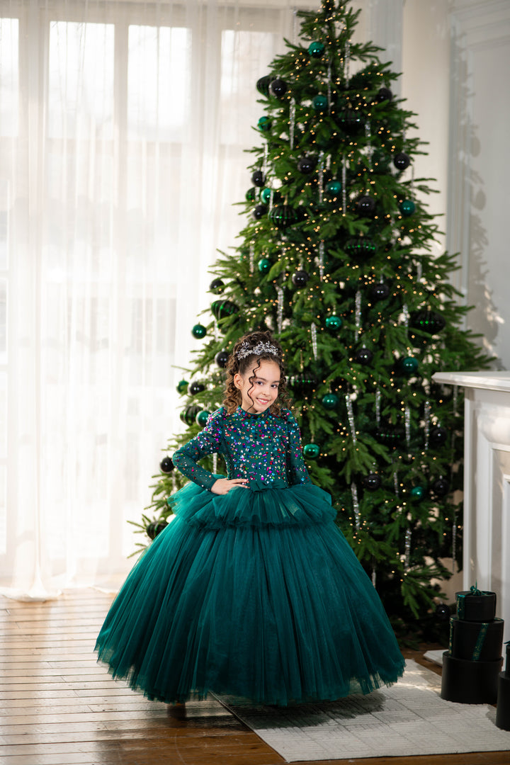 Child in a teal dress standing in front of a decorated Christmas tree.