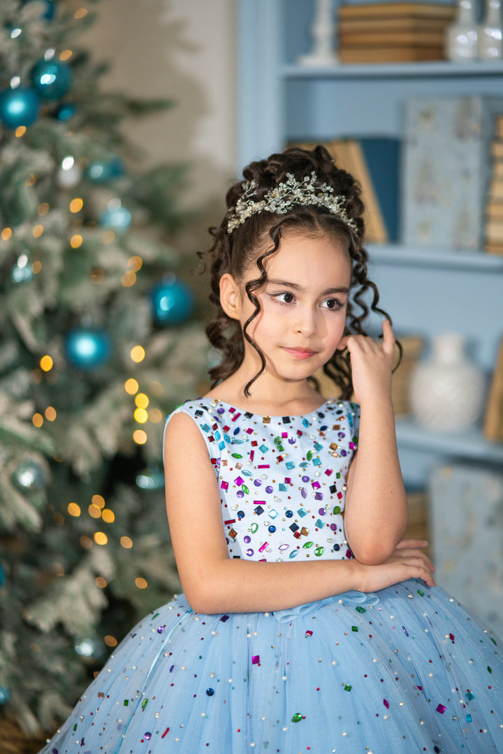 Young girl in a festive dress with a Christmas tree in the background