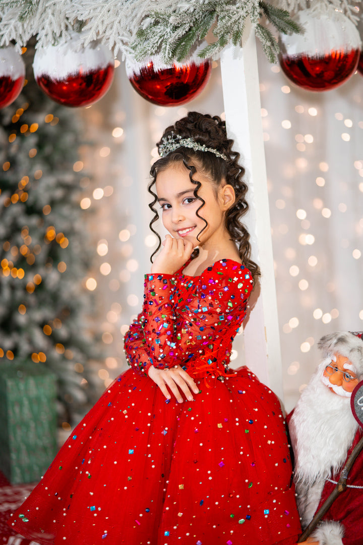 Young girl in a red dress standing in front of a Christmas tree with decorations.