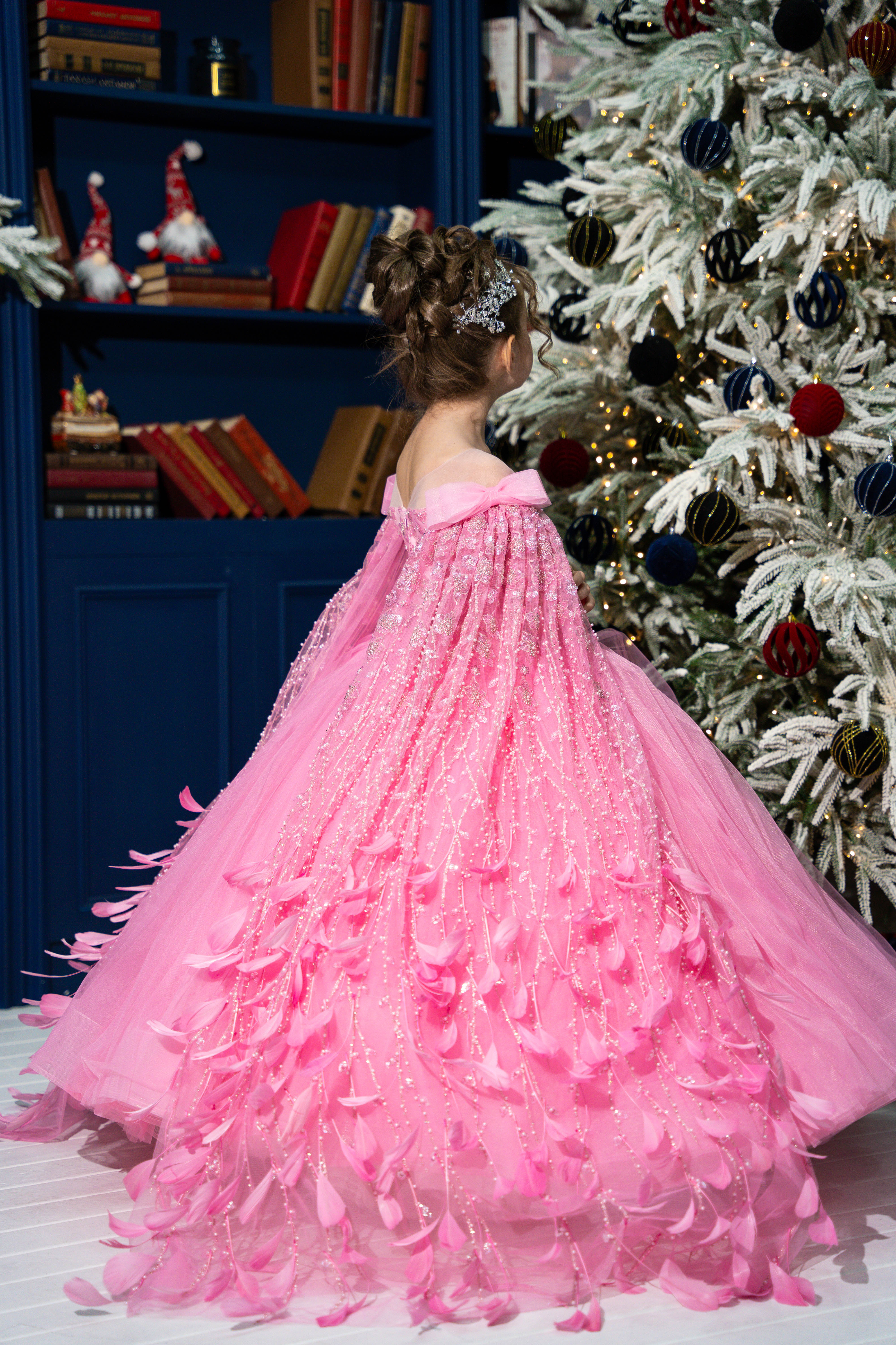 Child in a pink dress standing in front of a decorated Christmas tree.