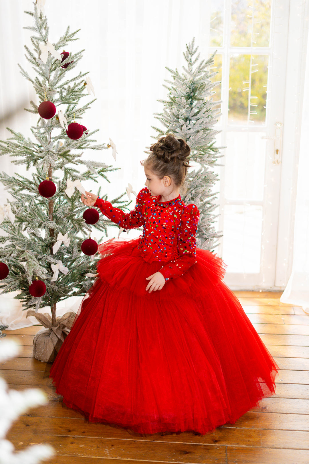 Child in a red dress standing next to a decorated Christmas tree.