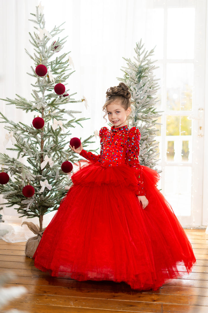 Young girl in a red dress standing next to a decorated Christmas tree.