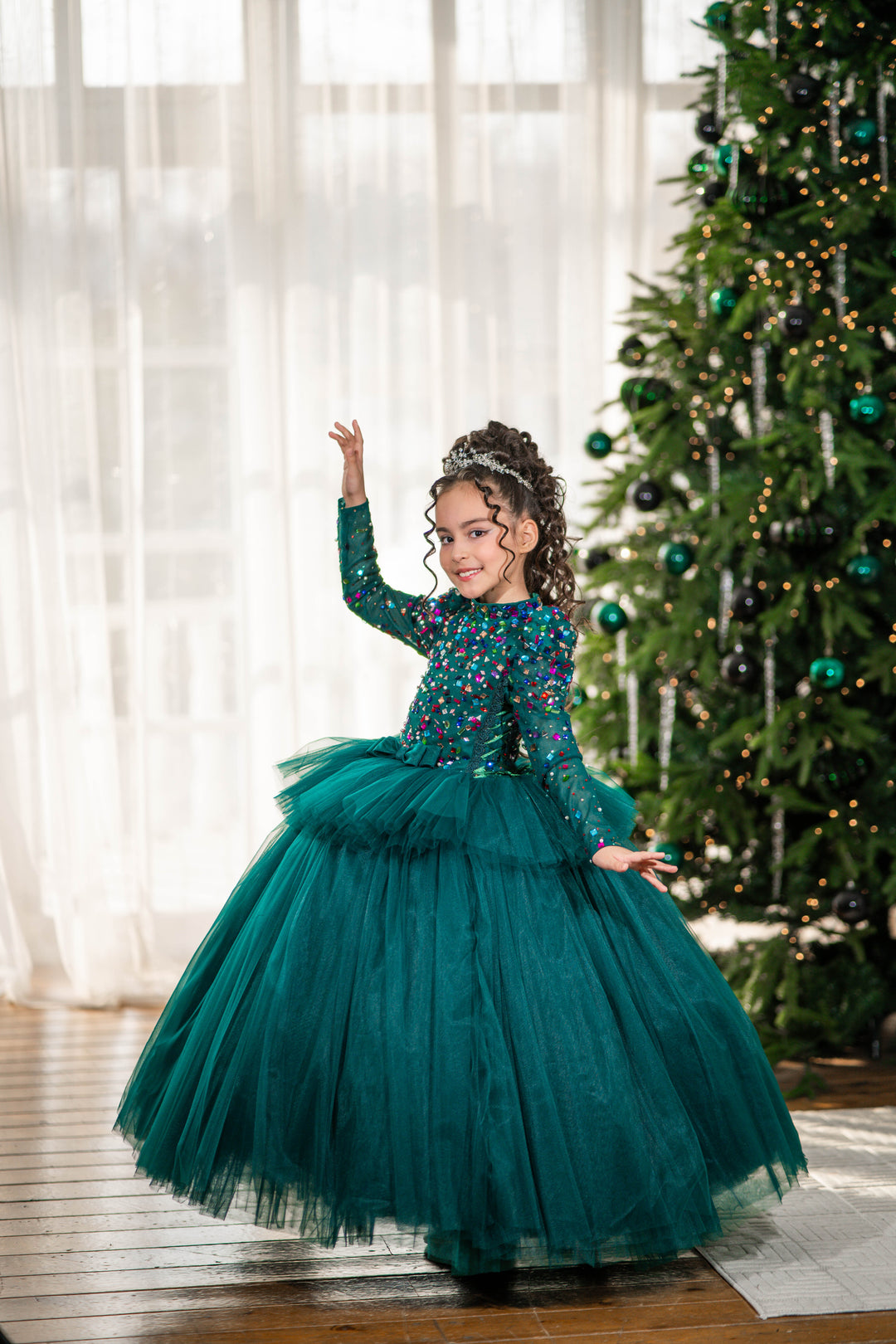 Young girl in a green dress standing in front of a decorated Christmas tree.