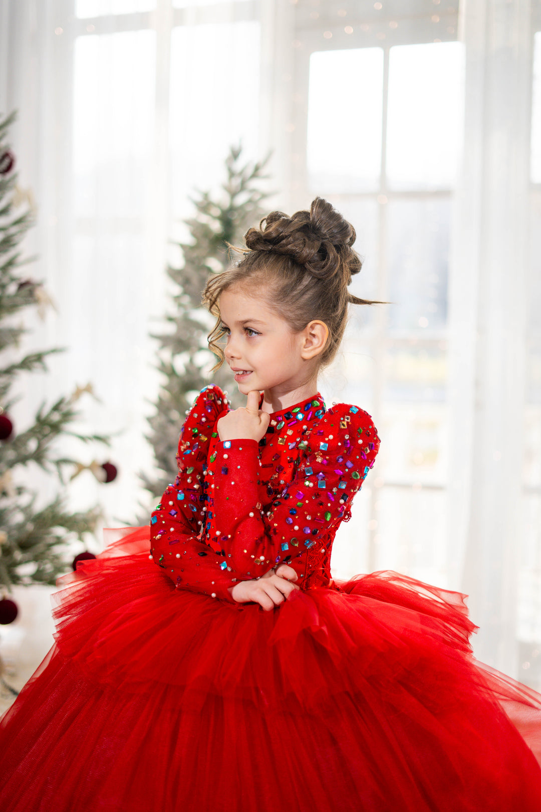 Young girl in a red dress with sequins and a tulle skirt, standing in front of a Christmas tree.
