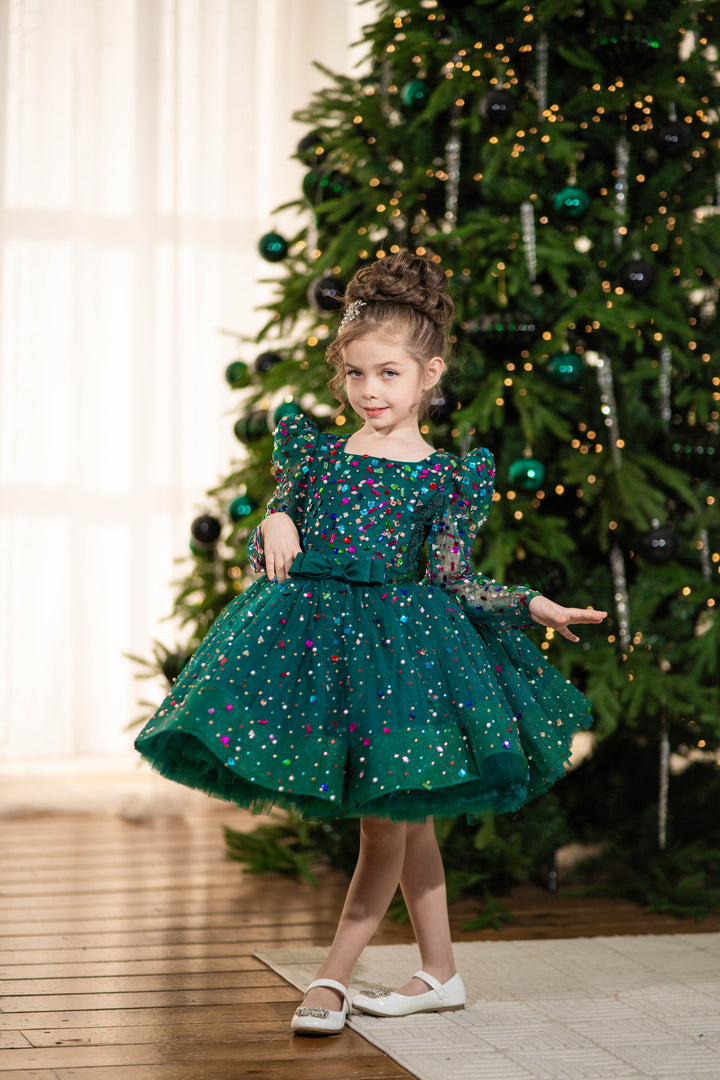 Young girl in a green dress standing in front of a decorated Christmas tree.