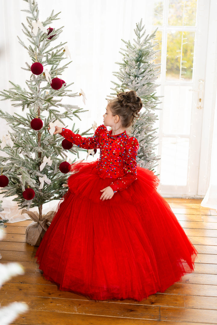 Young girl in a red dress standing next to a decorated Christmas tree.
