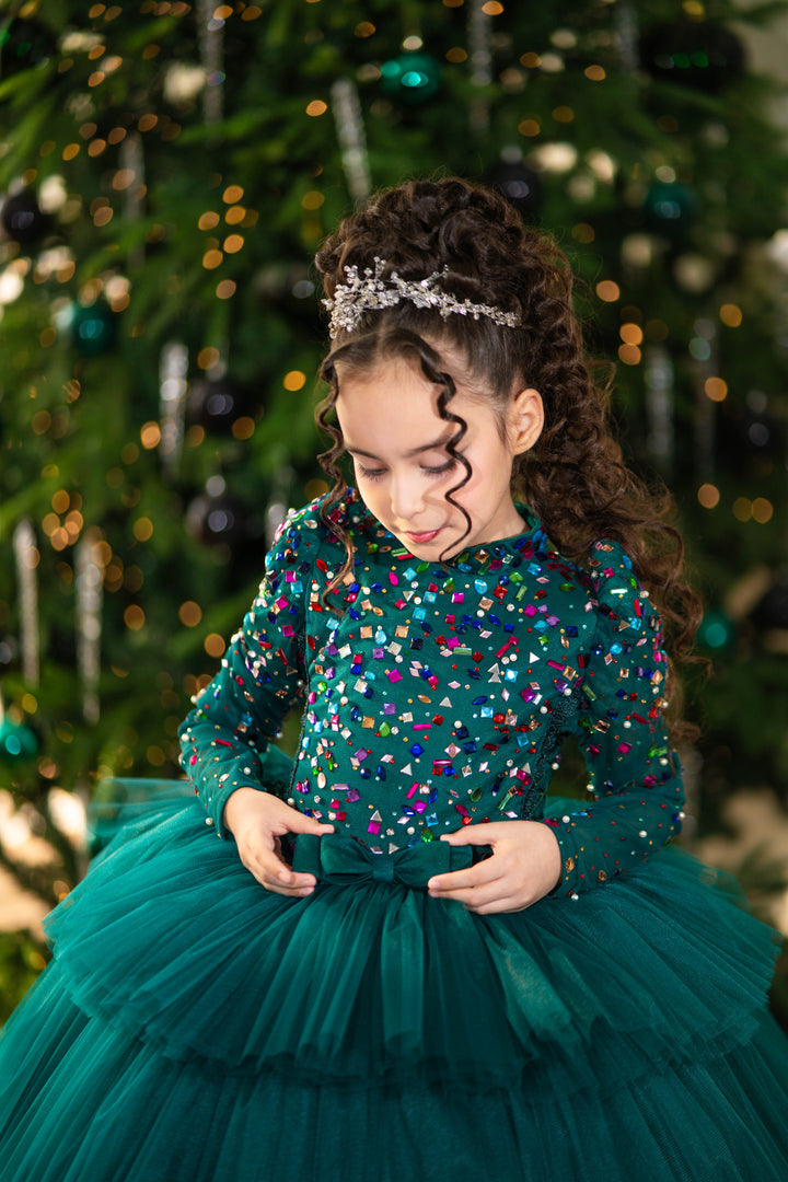 Young girl in a teal dress with colorful sequins standing in front of a decorated Christmas tree.