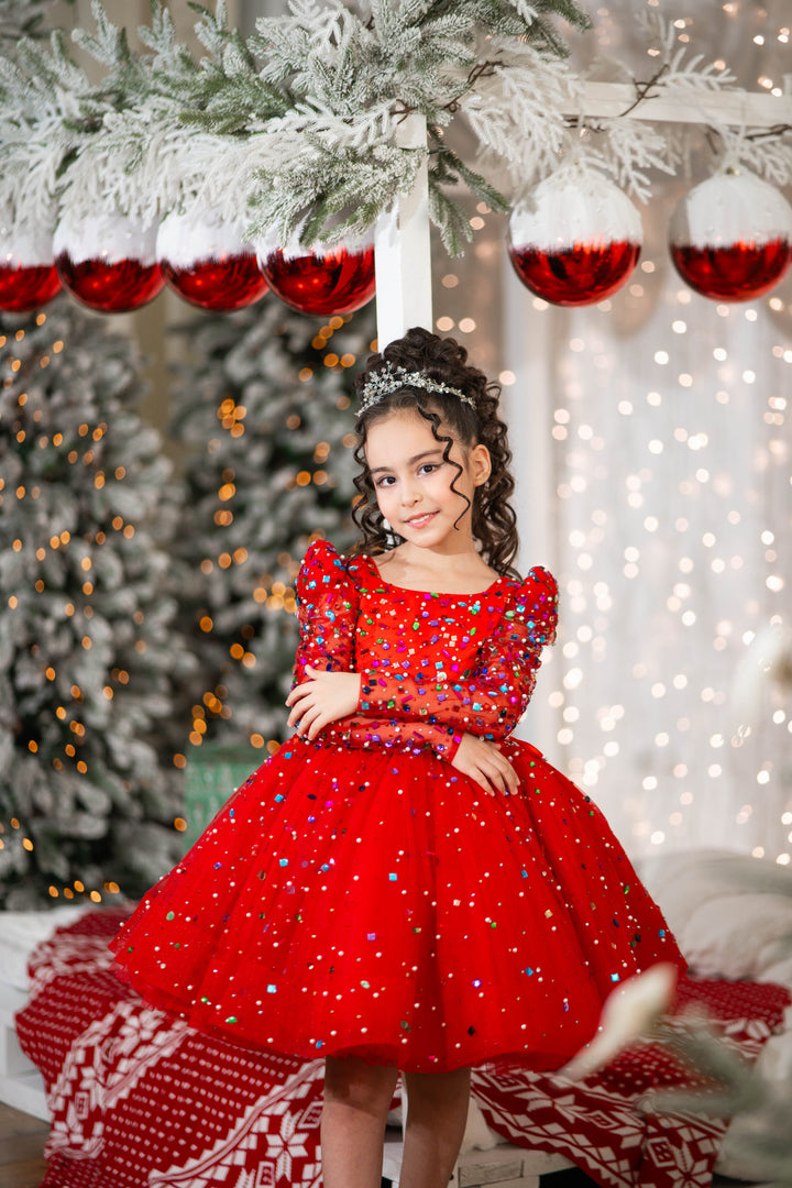 Young girl in a red dress with sequins sitting in front of a decorated Christmas tree.