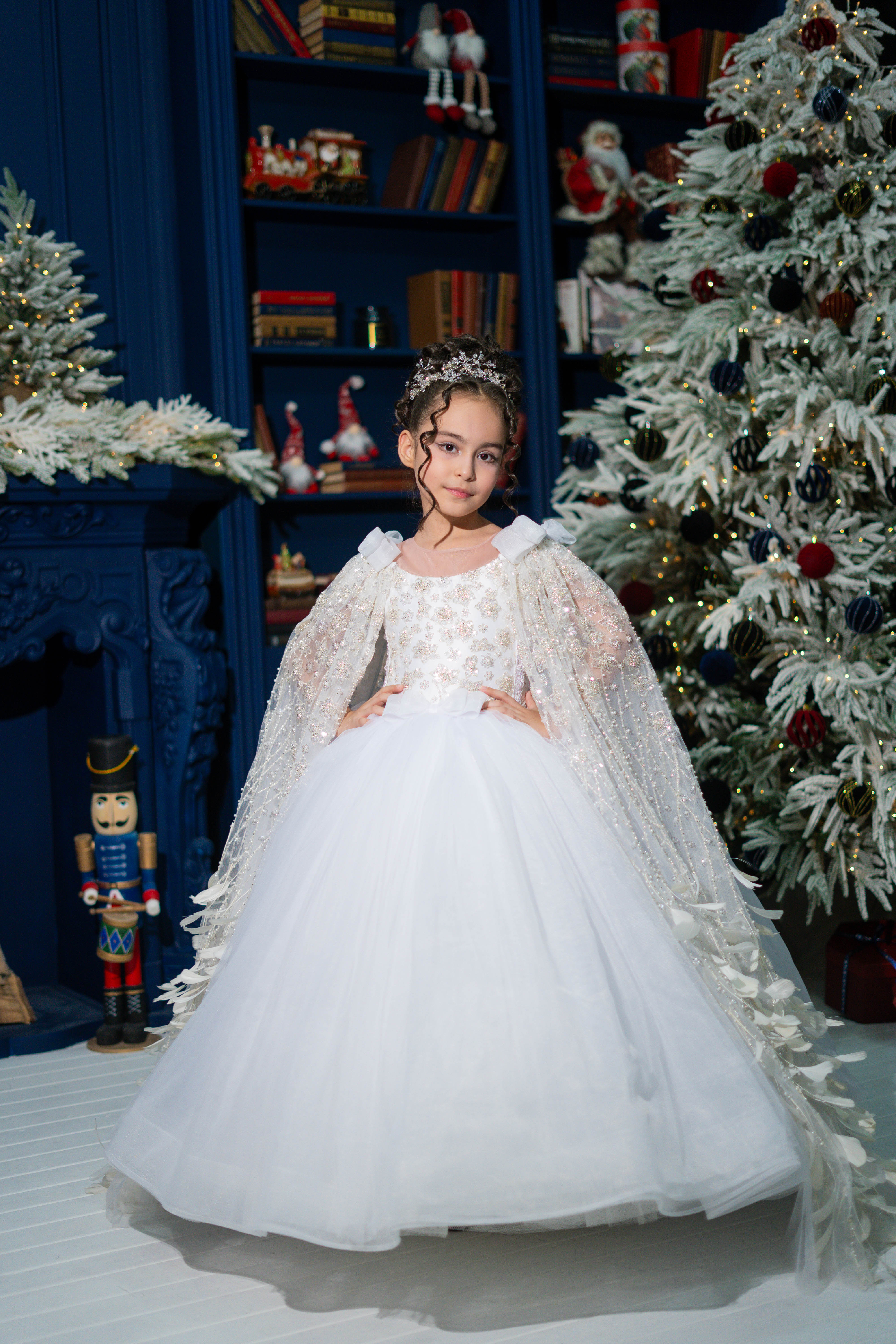 A girl in a white dress with a cape standing in front of Christmas decoration