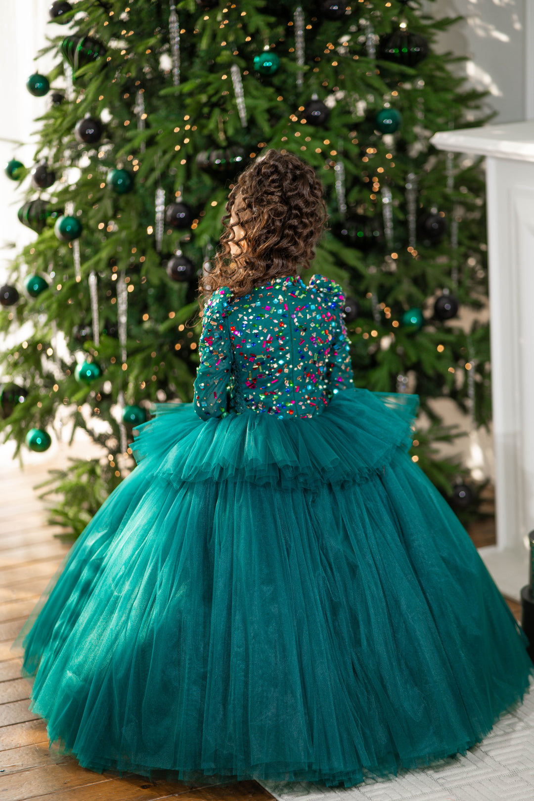 Child wearing a teal dress with a beaded top in front of a decorated Christmas tree.