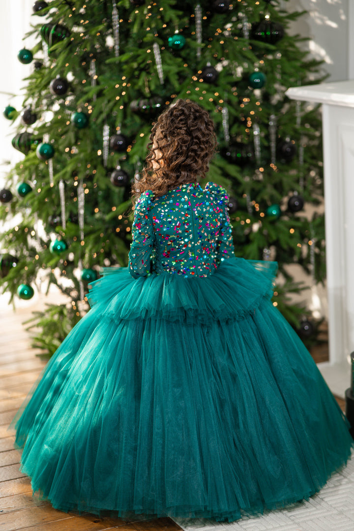 Child wearing a teal dress with a beaded top in front of a decorated Christmas tree.