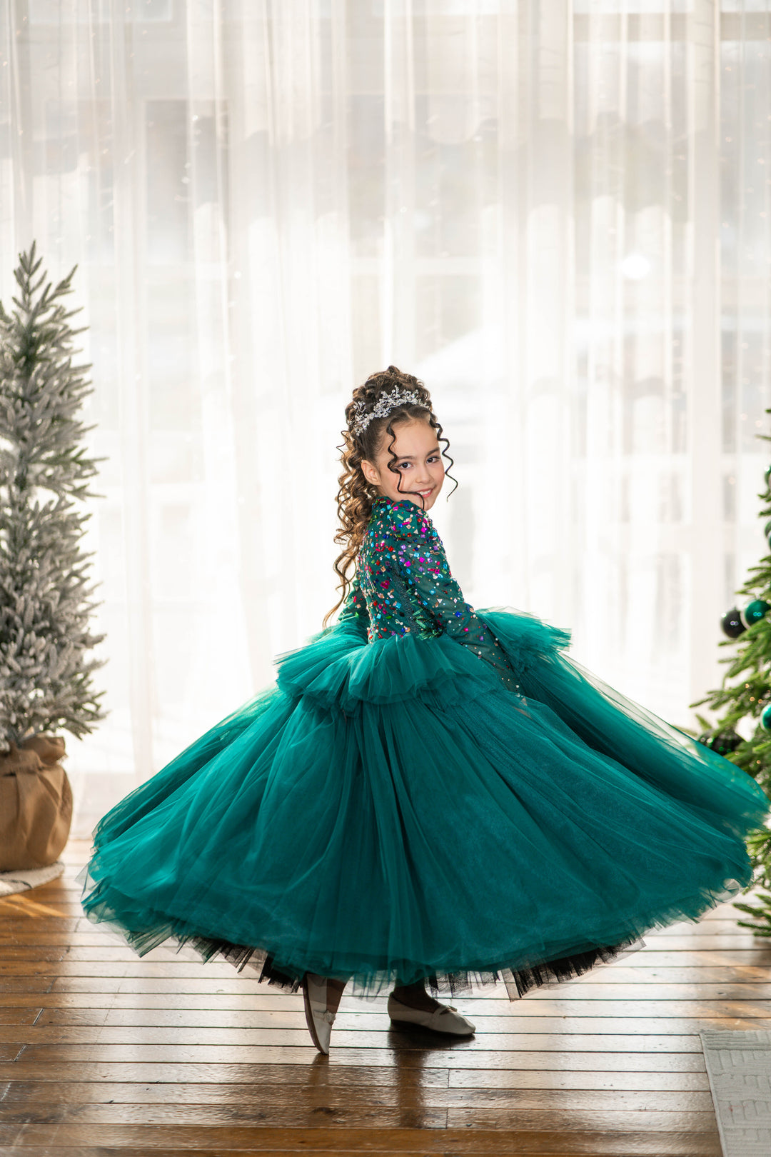 Child in a teal dress with floral top in a room with Christmas trees