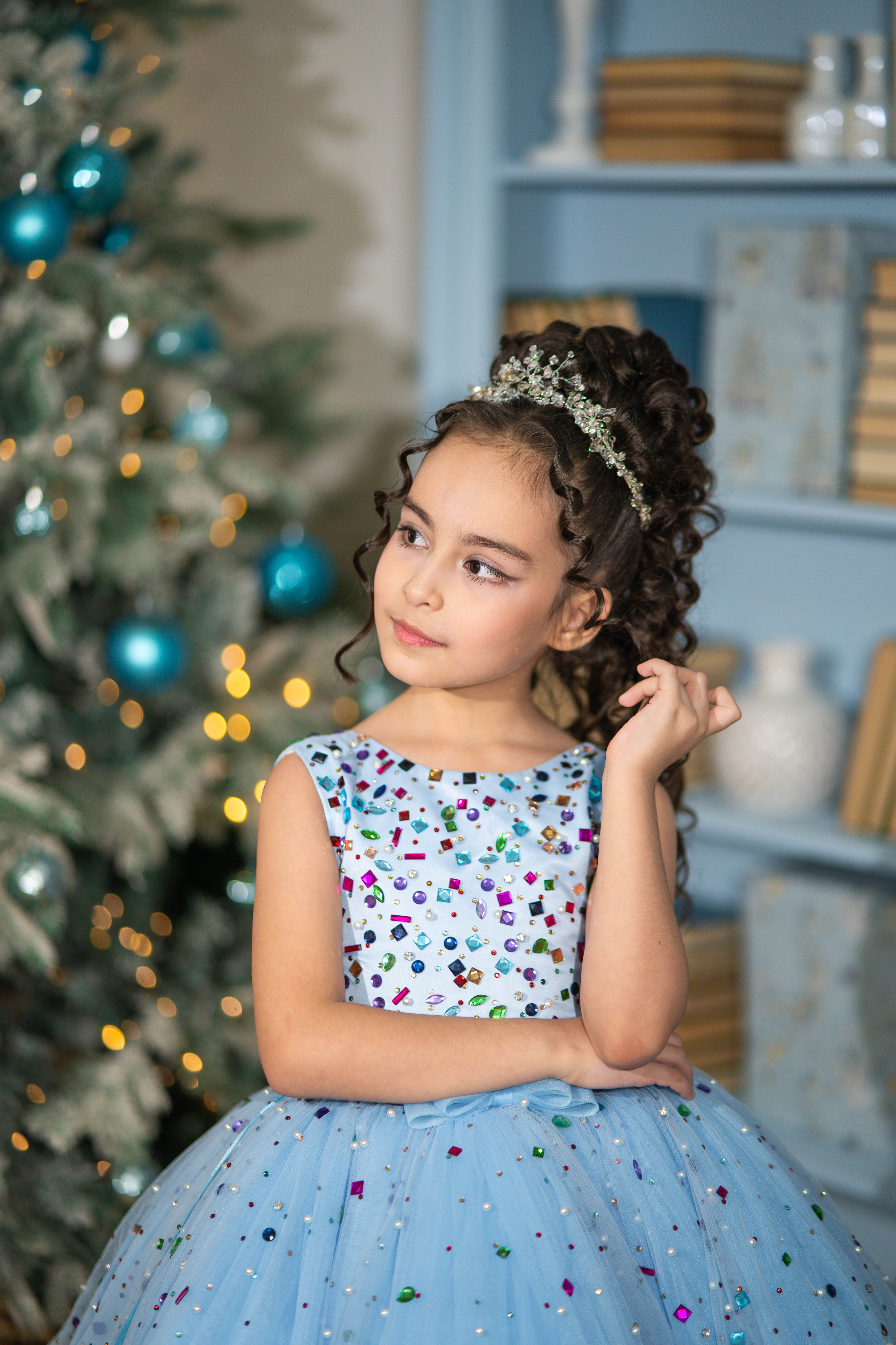 Young girl in a festive setting with a decorated tree and shelves in the background