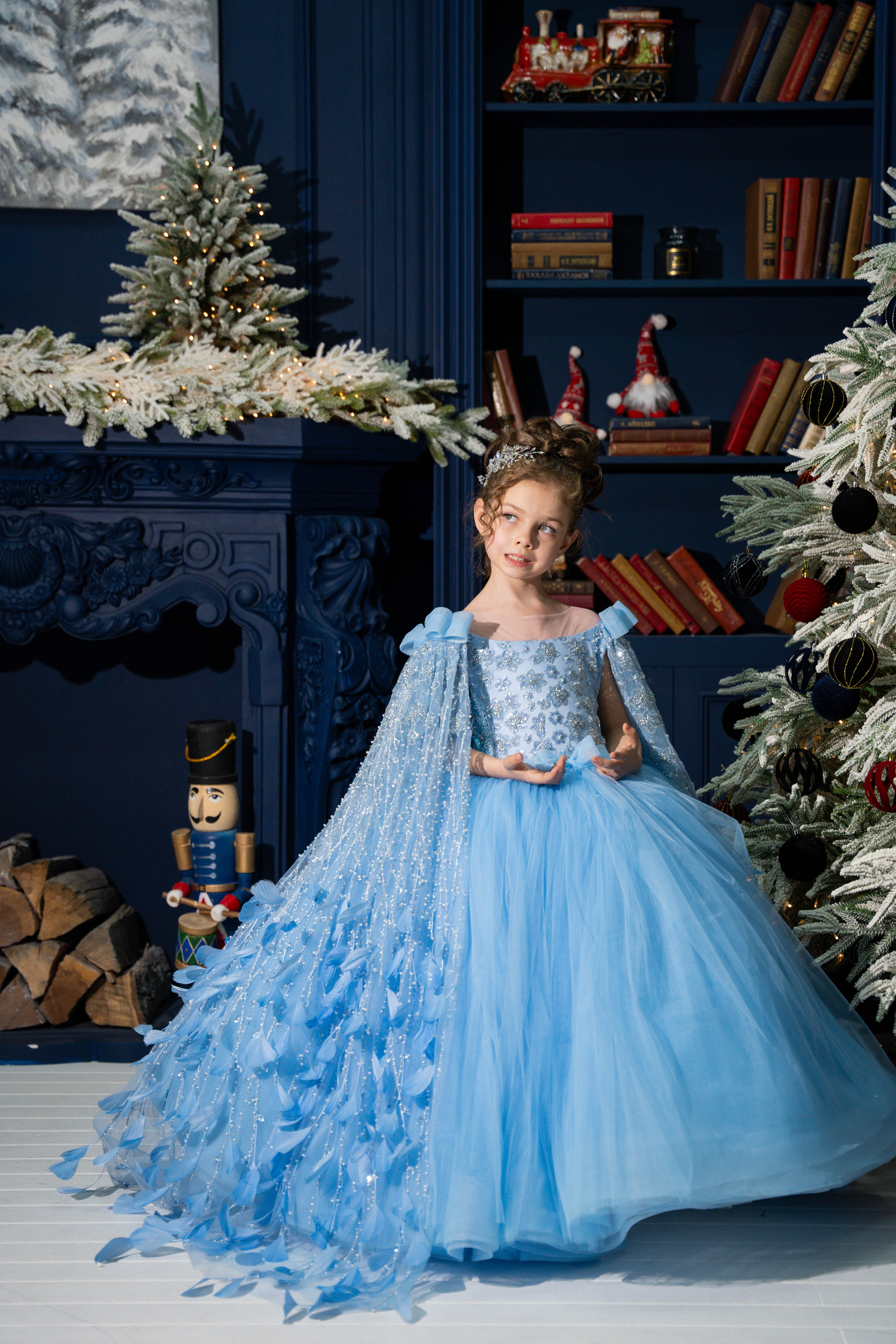 Young girl in a blue dress standing in a festive room with Christmas decorations.