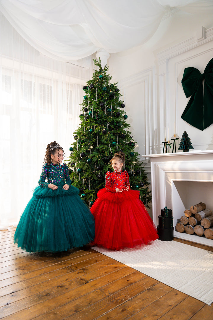 Two children in festive dresses standing in front of a decorated Christmas tree.