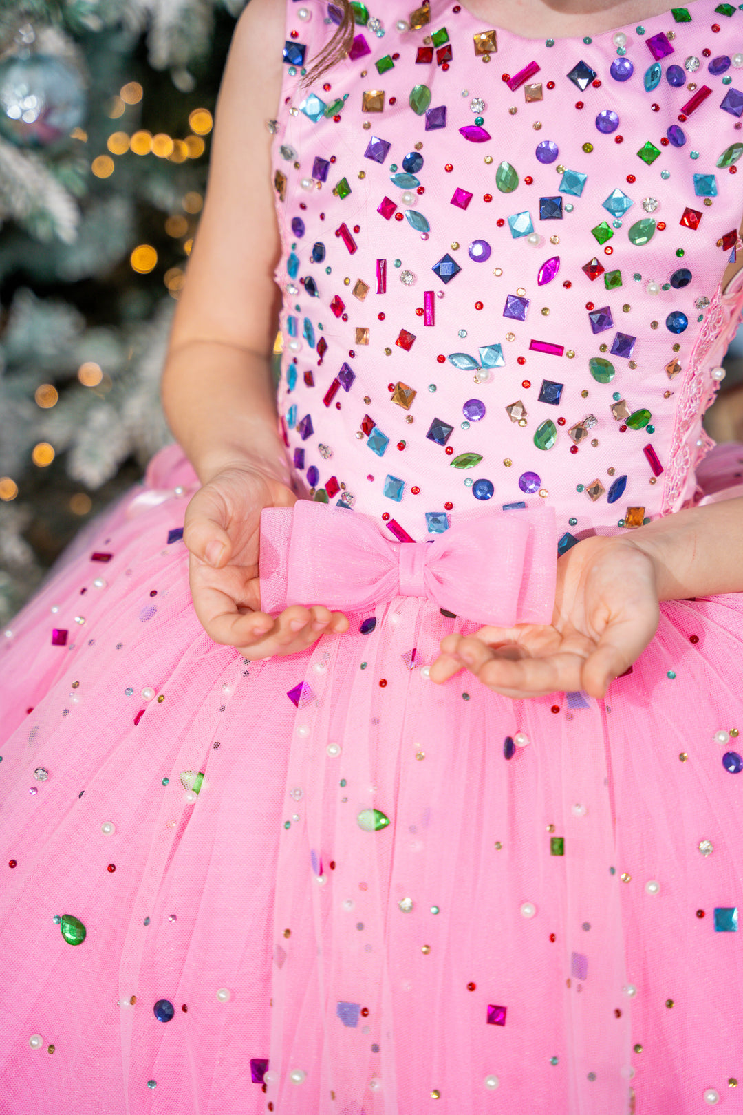 Baby Pink dress with colorful sequin pattern worn by a child, blurred Christmas tree in the background