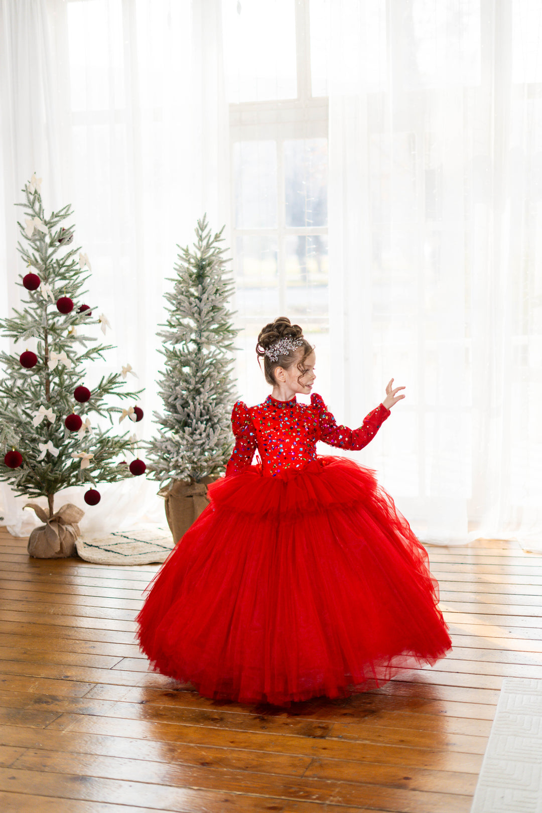 Child in a red dress standing in a room with Christmas trees.