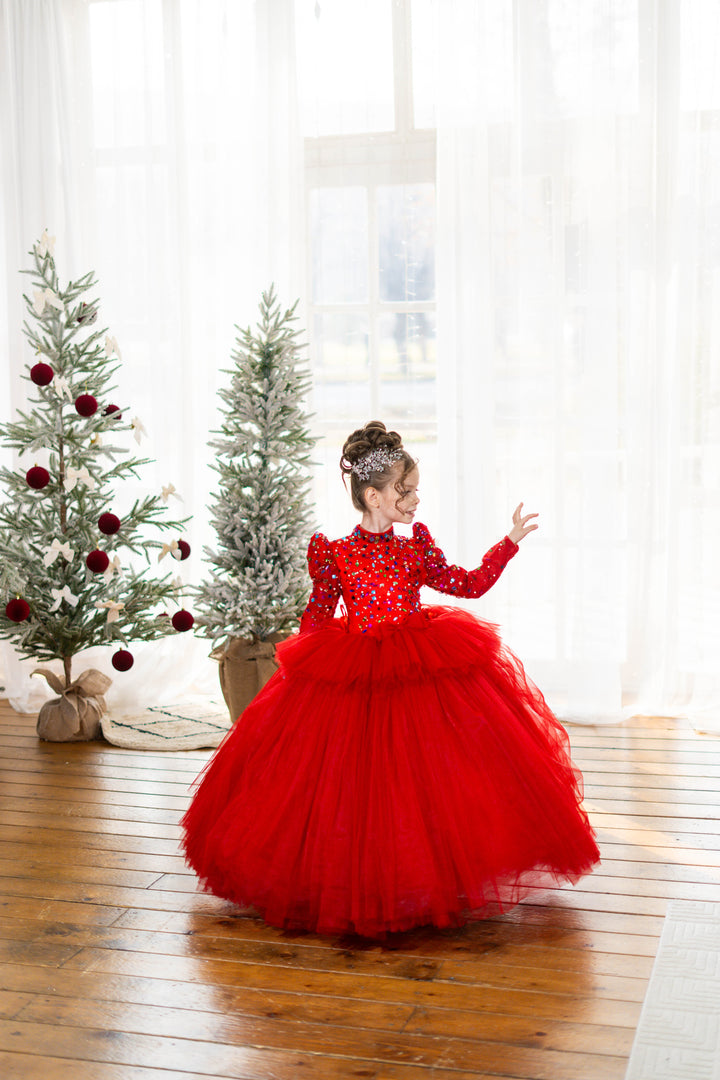 Child in a red dress standing in a room with Christmas trees.