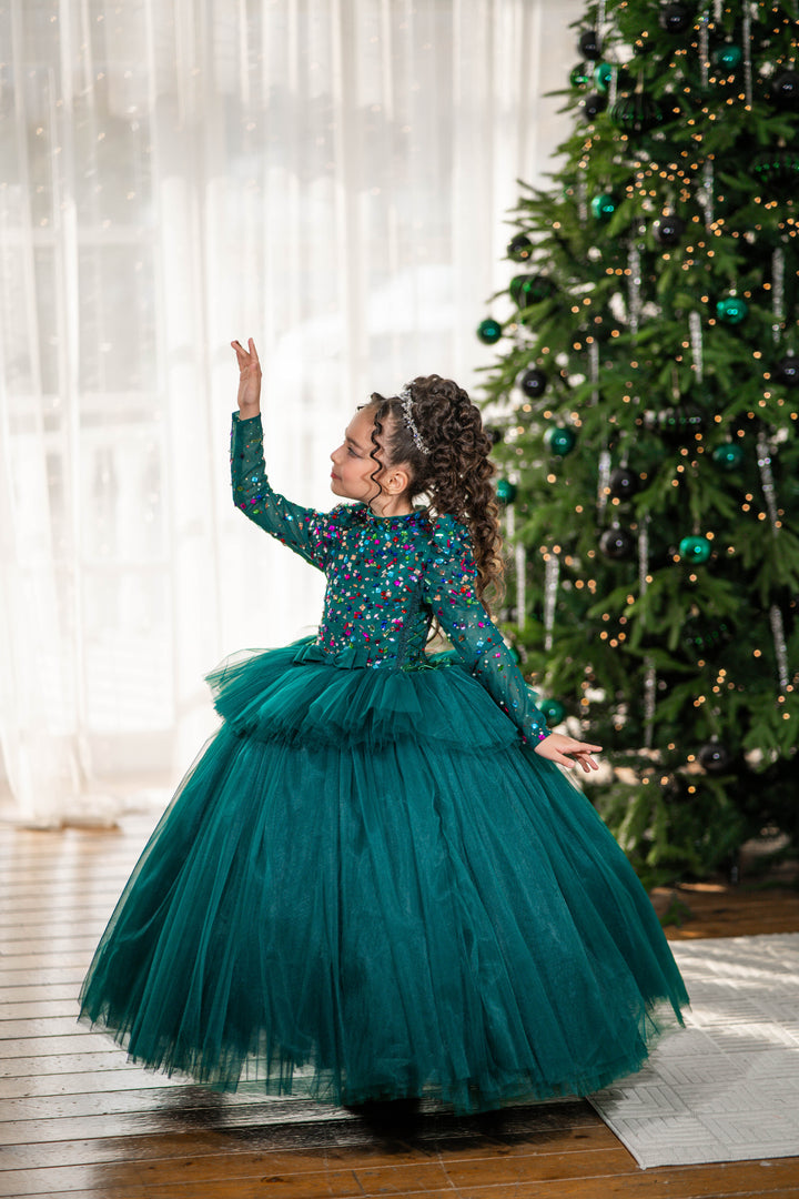 Young girl in a green dress standing in front of a decorated Christmas tree.