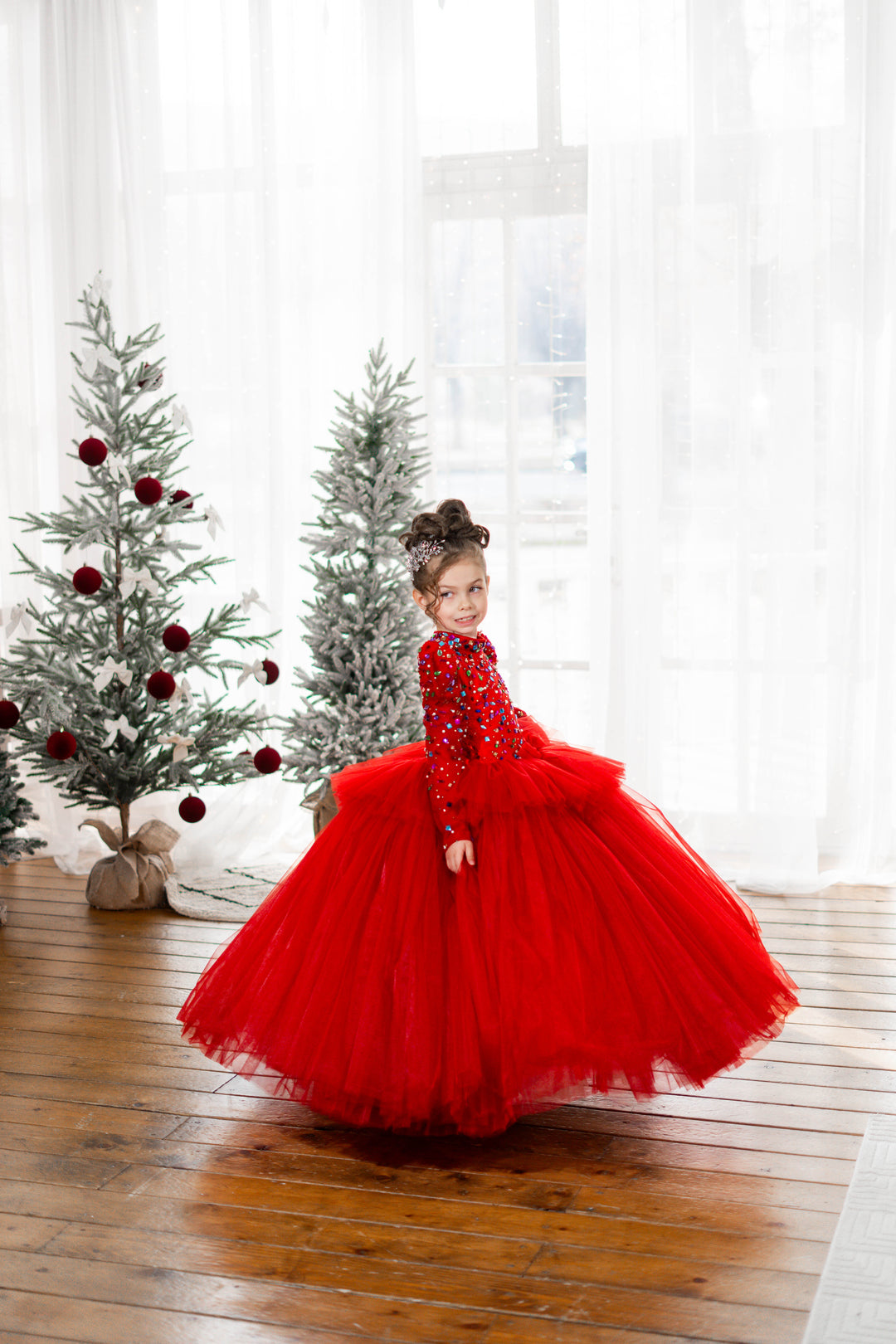 A girl in a red dress standing in front of Christmas trees.