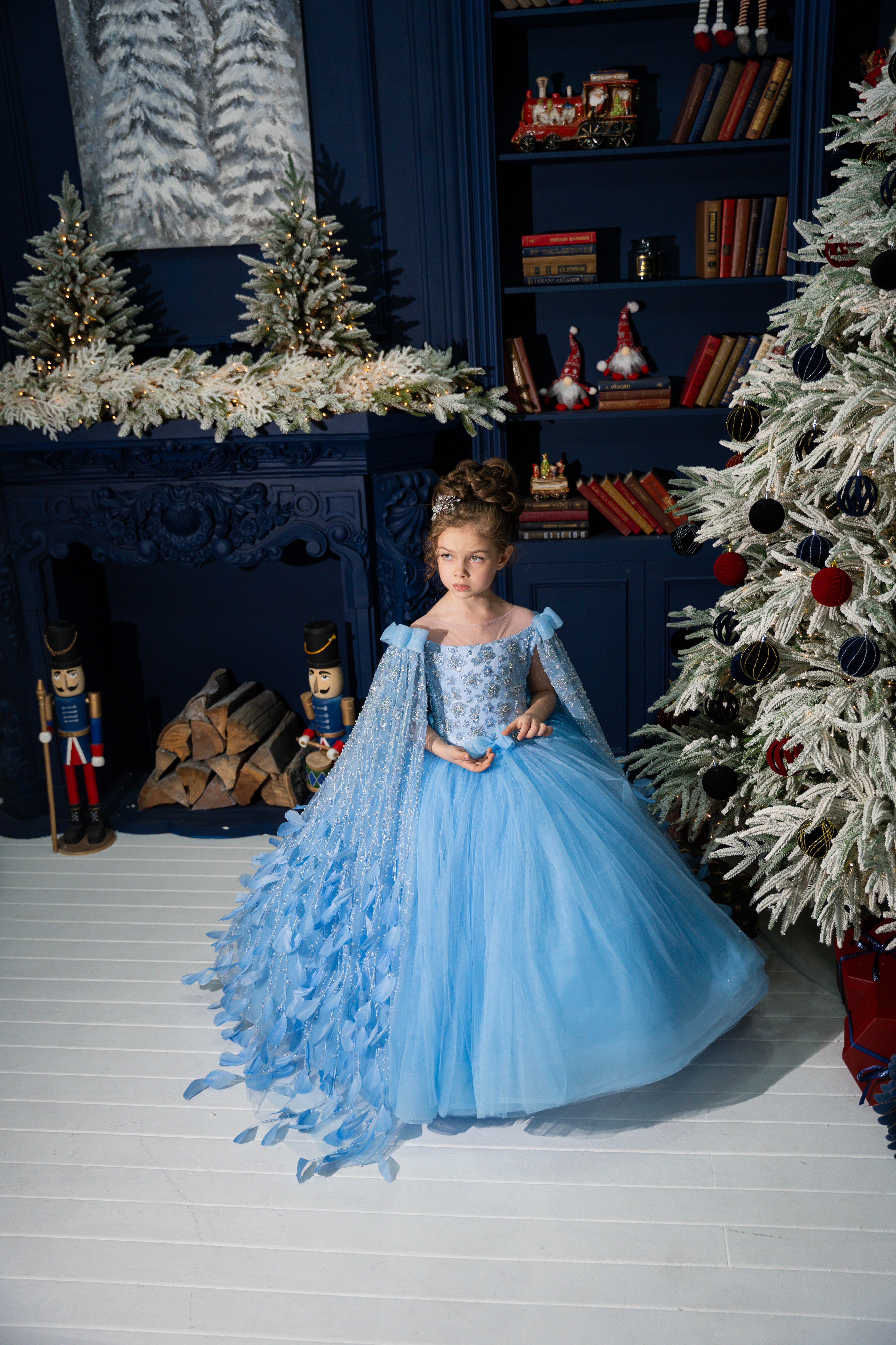 Young girl in a blue dress standing in a festive room with Christmas decorations.