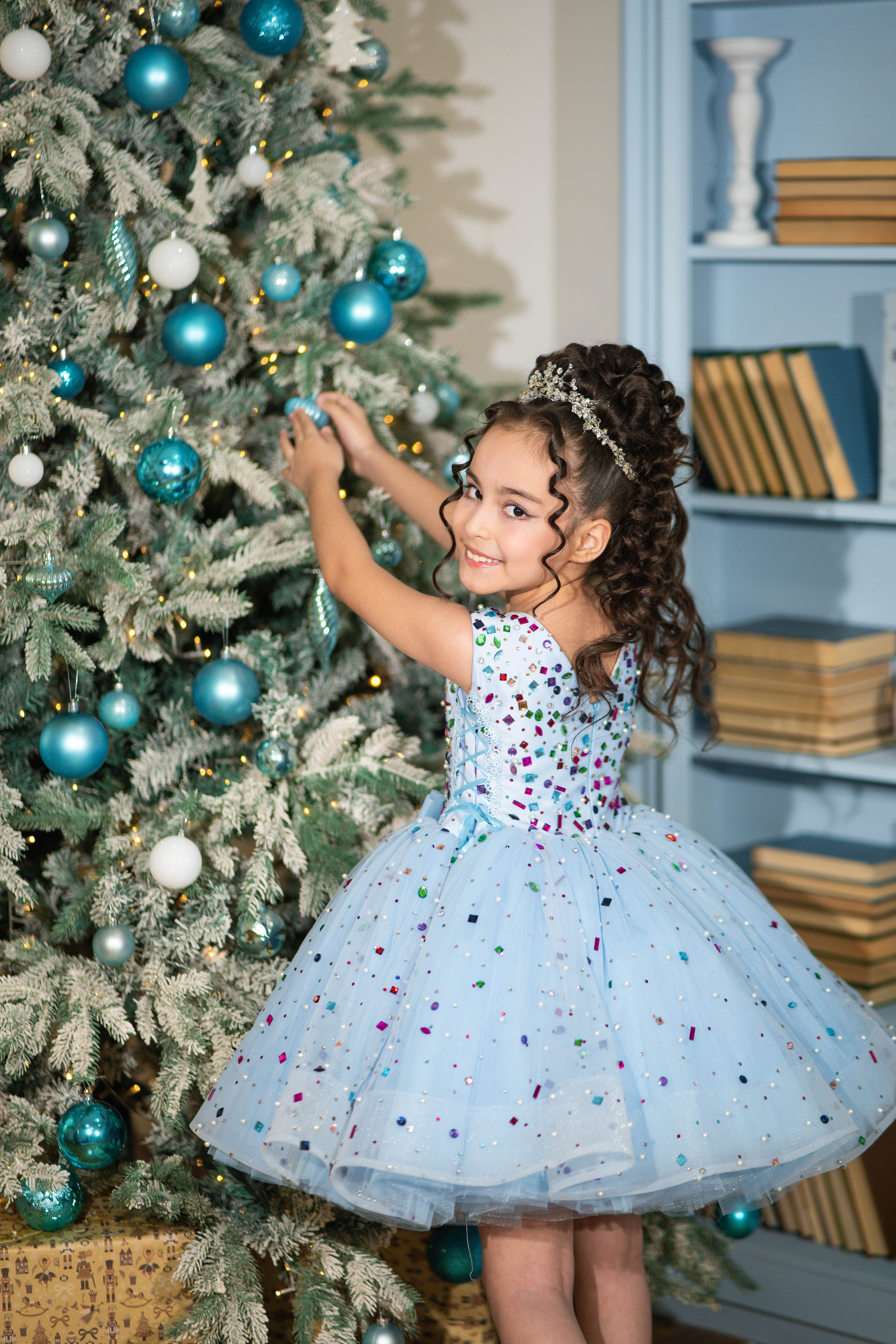 Young girl in a festive dress standing next to a decorated Christmas tree.