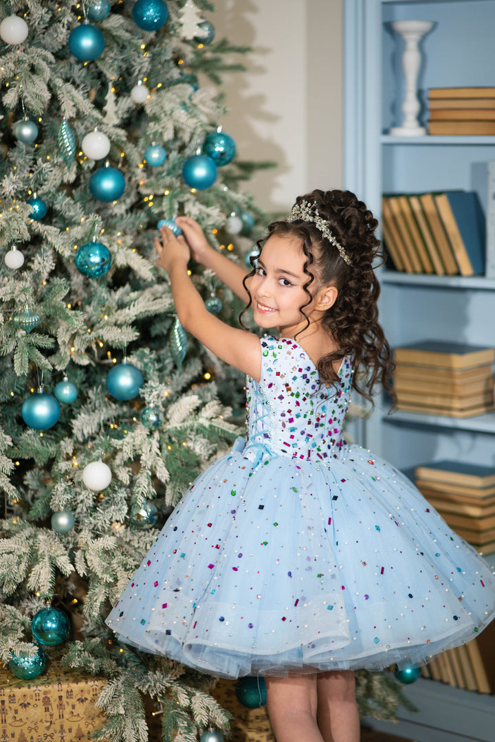 Young girl in a festive dress standing next to a decorated Christmas tree.