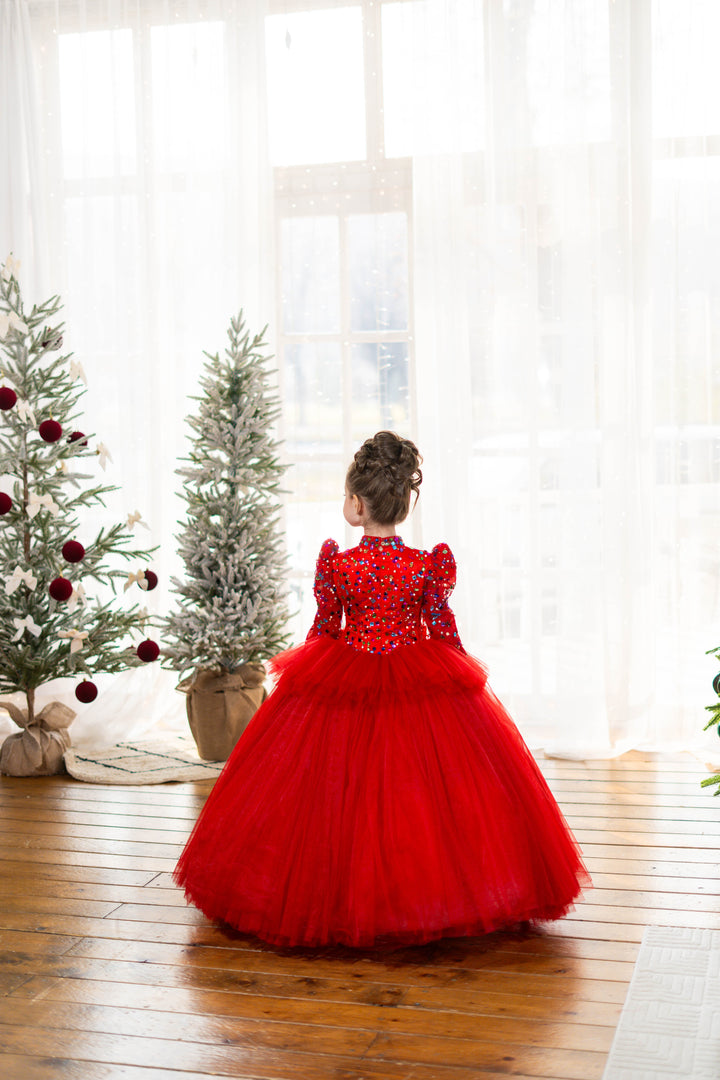 Young girl in a red dress standing in front of Christmas trees with white curtains.