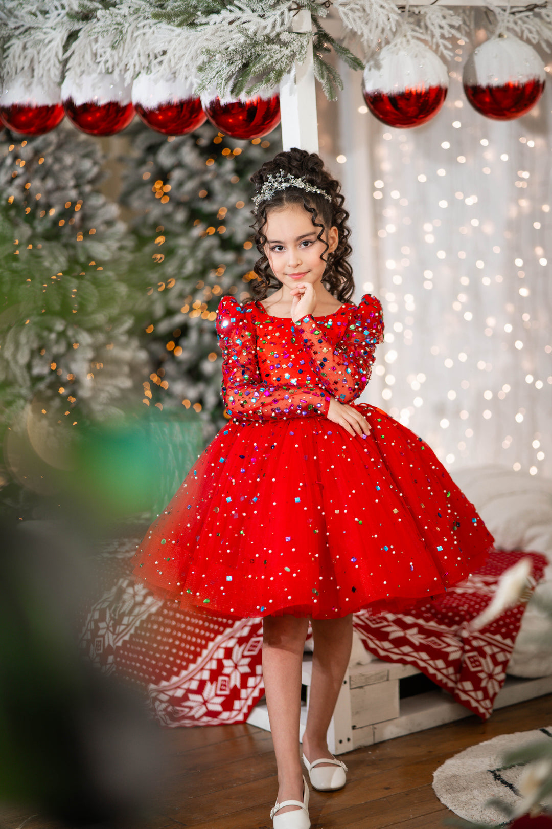 Young girl in a red dress with sequins standing in a festive setting with Christmas decorations.