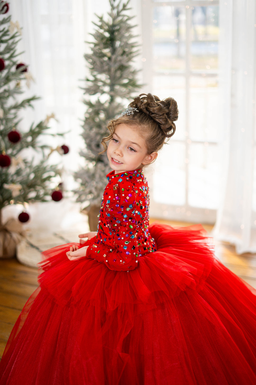 Young girl in a red dress with sequins standing in front of Christmas trees.