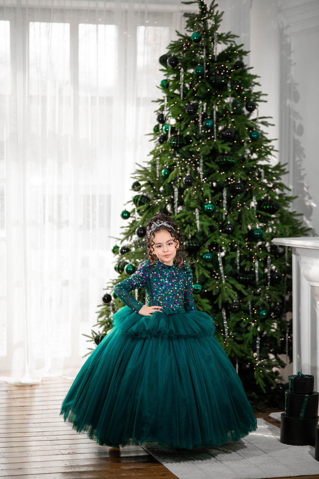 Young girl in a green dress standing in front of a decorated Christmas tree.