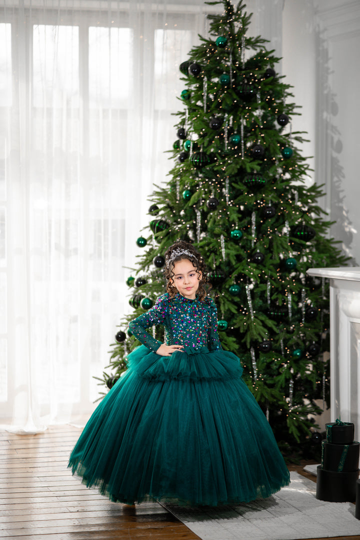 Young girl in a green dress standing in front of a decorated Christmas tree.