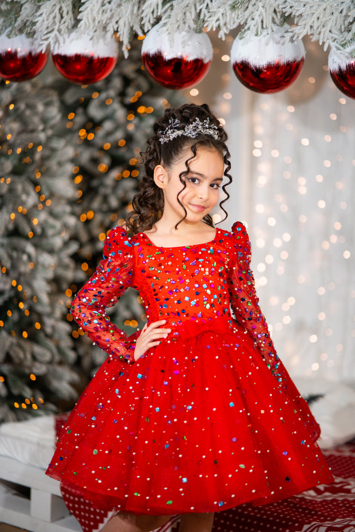 Young girl in a red dress with sequins standing in front of a decorated Christmas tree.