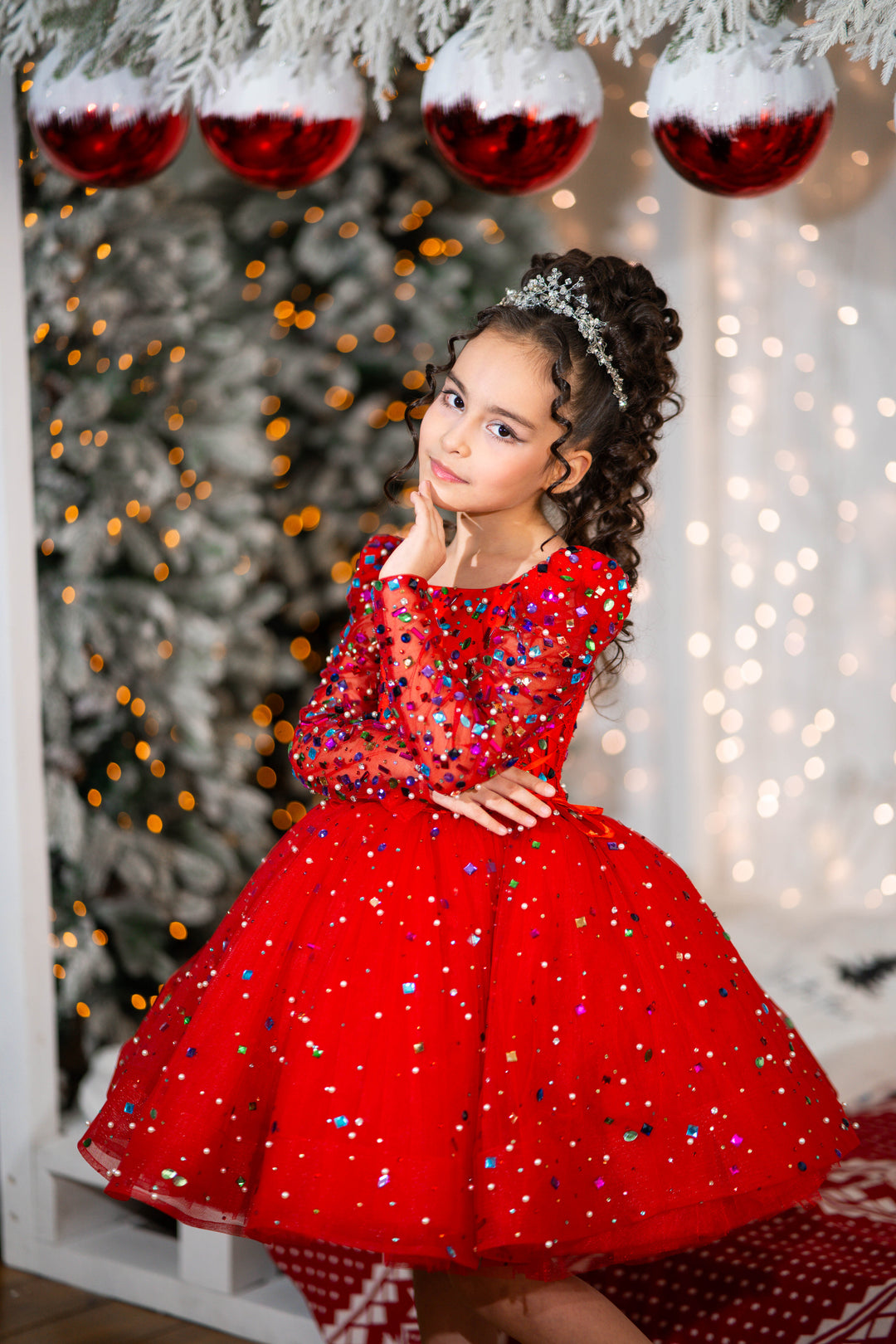 Young girl in a red dress with sequins standing in front of a decorated Christmas tree.