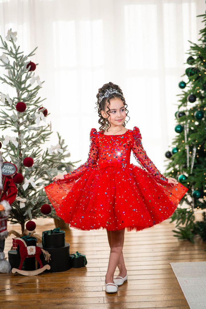 Baby girl in a red dress standing between two decorated Christmas trees.