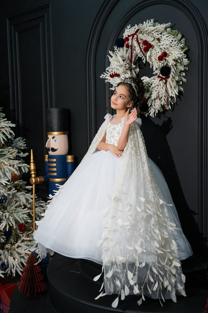 A child in a white dress with a decorative wreath and Christmas tree in the background