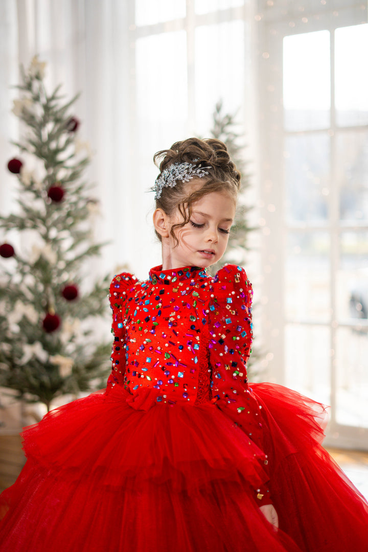 Baby girl in a red dress with sequins and tulle, standing in a room with a decorated Christmas tree.