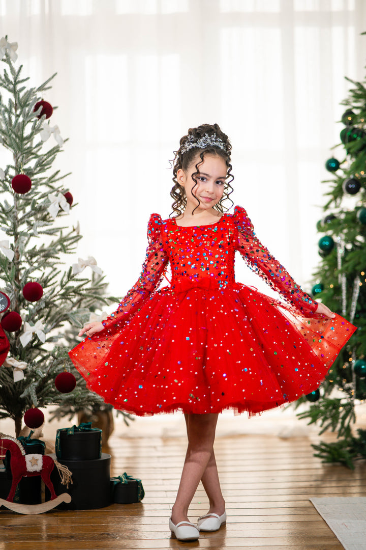 Baby girl in a red dress standing between two decorated Christmas trees.